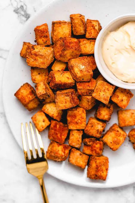 Tofu croutons served with cream paste on a white plate with a silver fork.