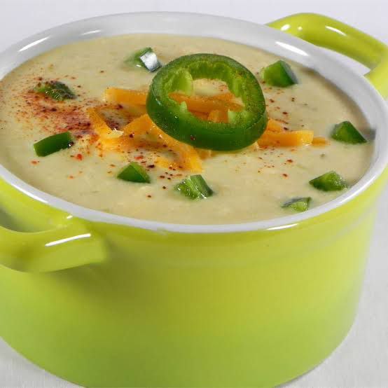 The perfect cream of jalapeno soup with sliced jalapenos and garnished with other spices on a neon green pot.