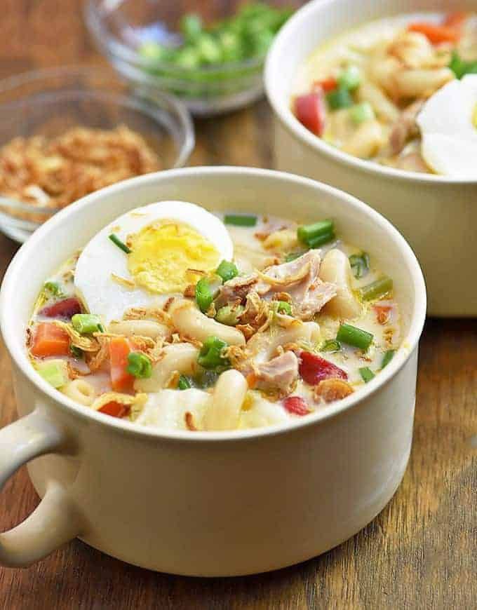 Macaroni and celery cream soup in a white bowl with sliced eggs and other vegetables on top.