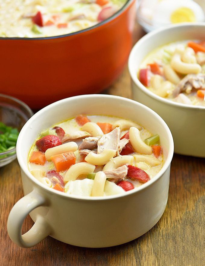 A white bowl of soup with hotdogs and other vegetables as a topping.